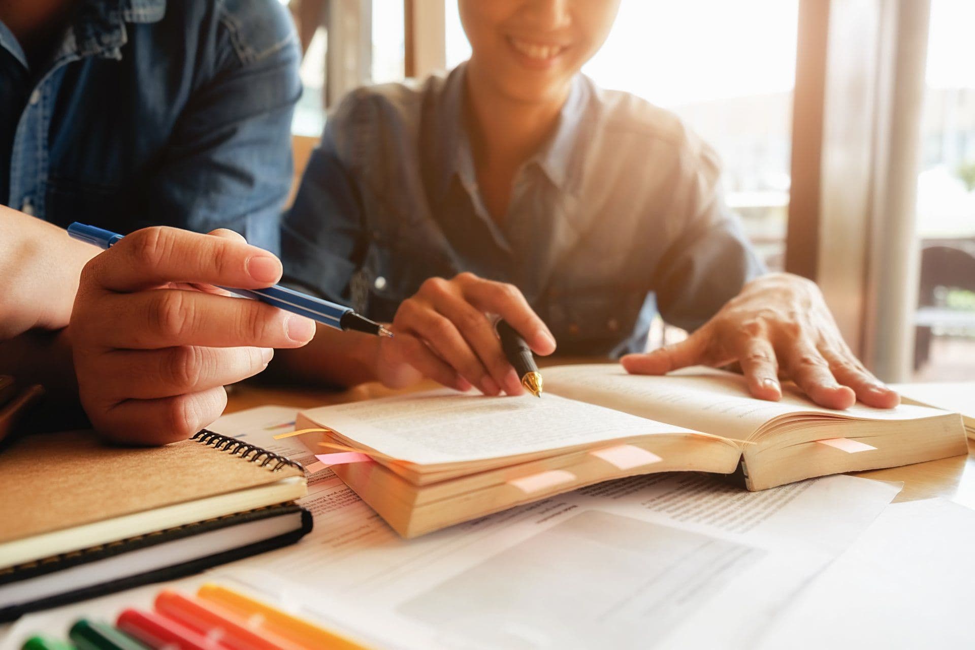 Dos estudiantes estudiando con un libro abierto y una libreta